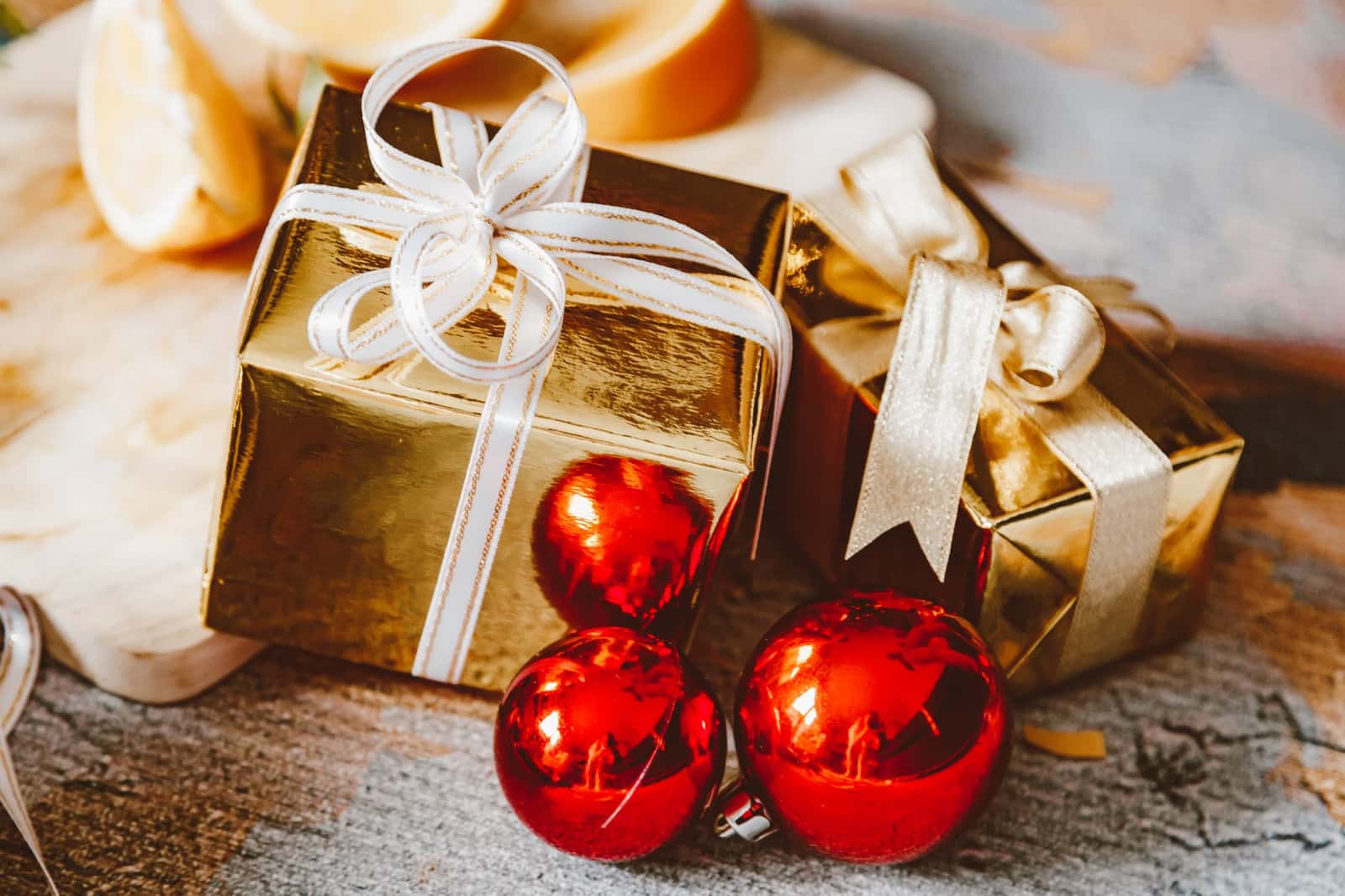Gold wrapped gift boxes with white ribbon beside red holiday baubles